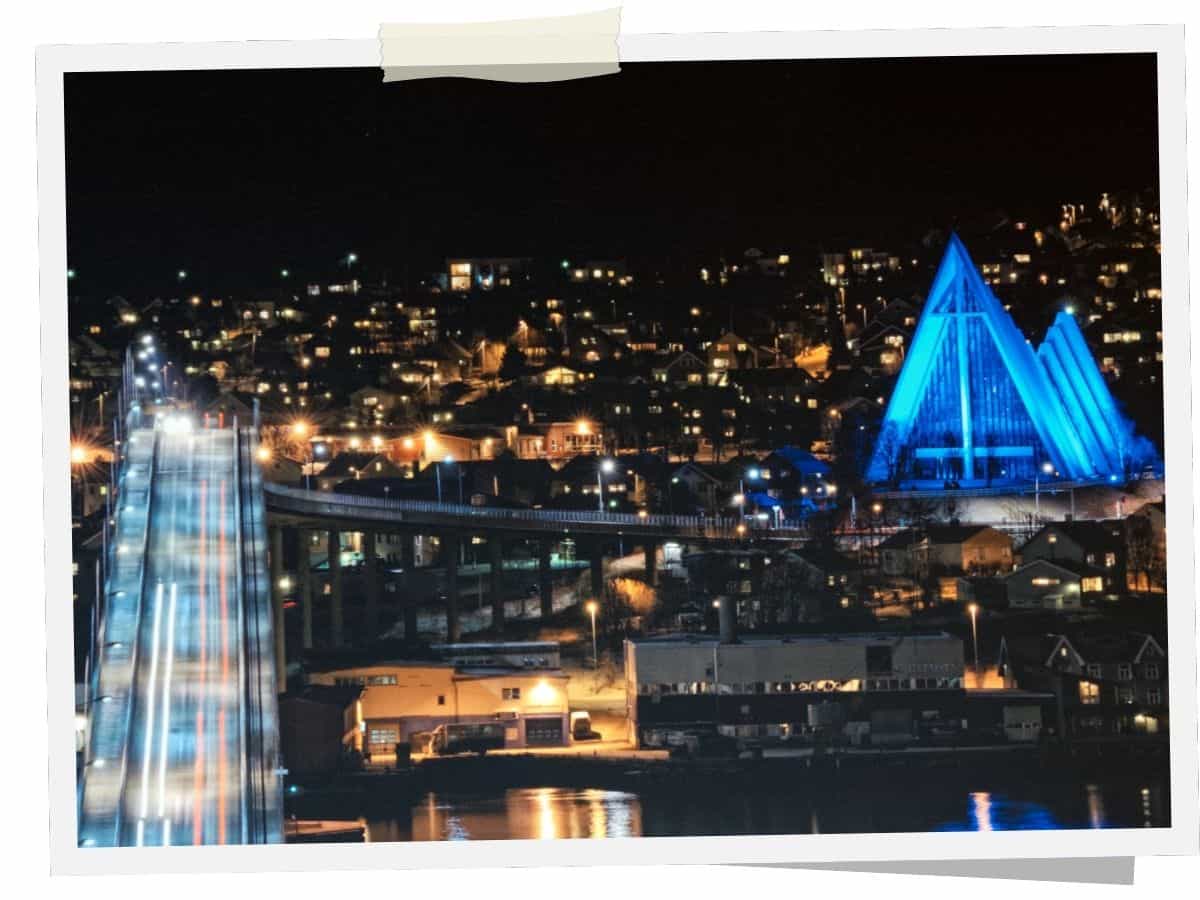 Beleuchtete Eismeerkathedrale in Tromsø bei Nacht mit Tromsøbrücke im Vordergrund