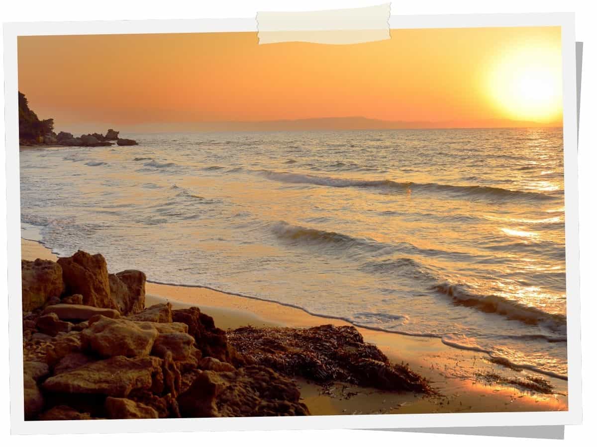 Sonnenuntergang über dem Ionischen Meer bei Kyllini im Westen des Peloponnes in Griechenland mit sanften Wellen, Sandstrand und felsiger Küste.